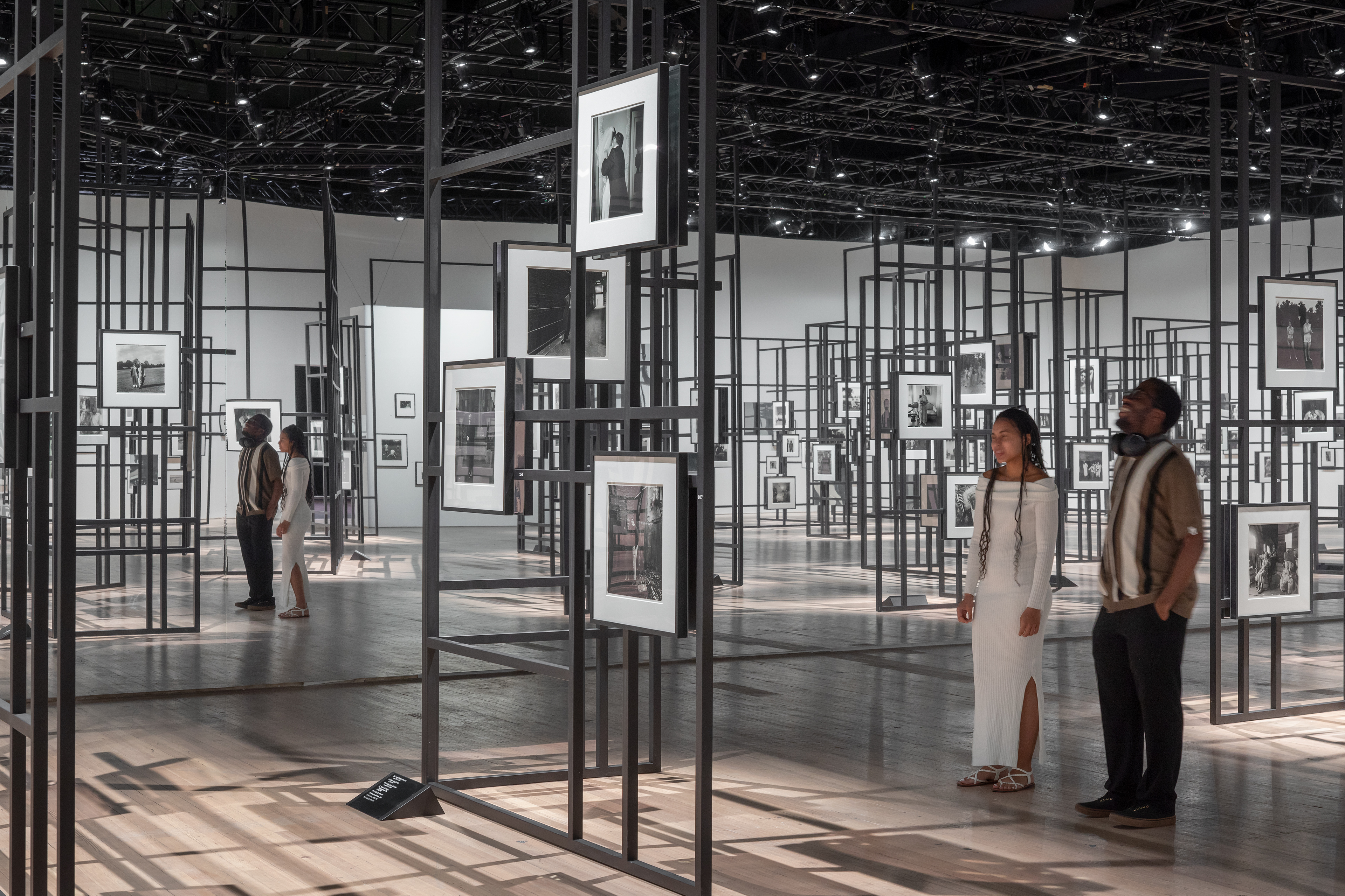 Visitors wander among a group of Diane Arbus photographs, hung and arranged on an intricate scaffolding system.