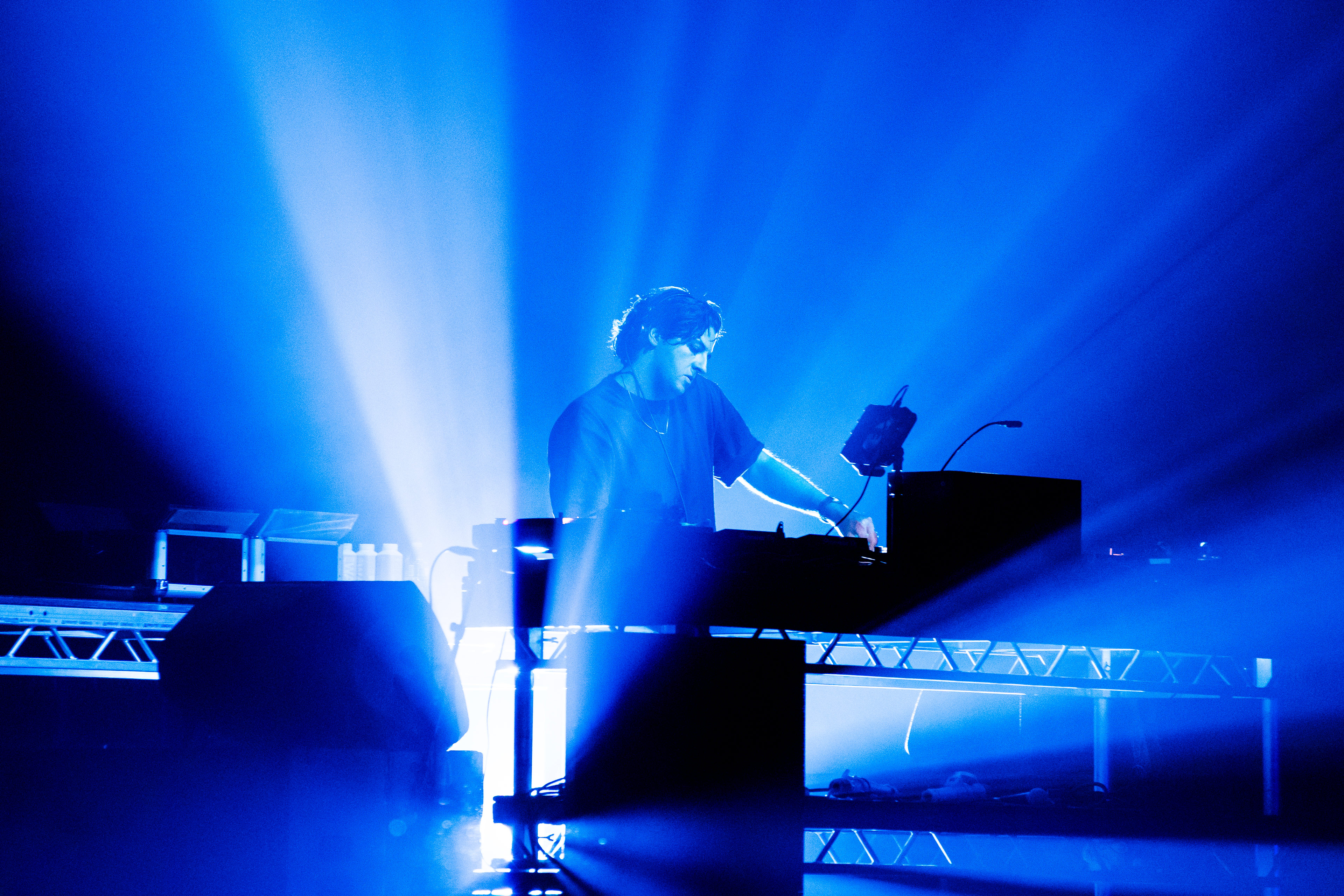 Jamie xx performing in the Drill Hall against a backdrop of dramatic blue lighting.