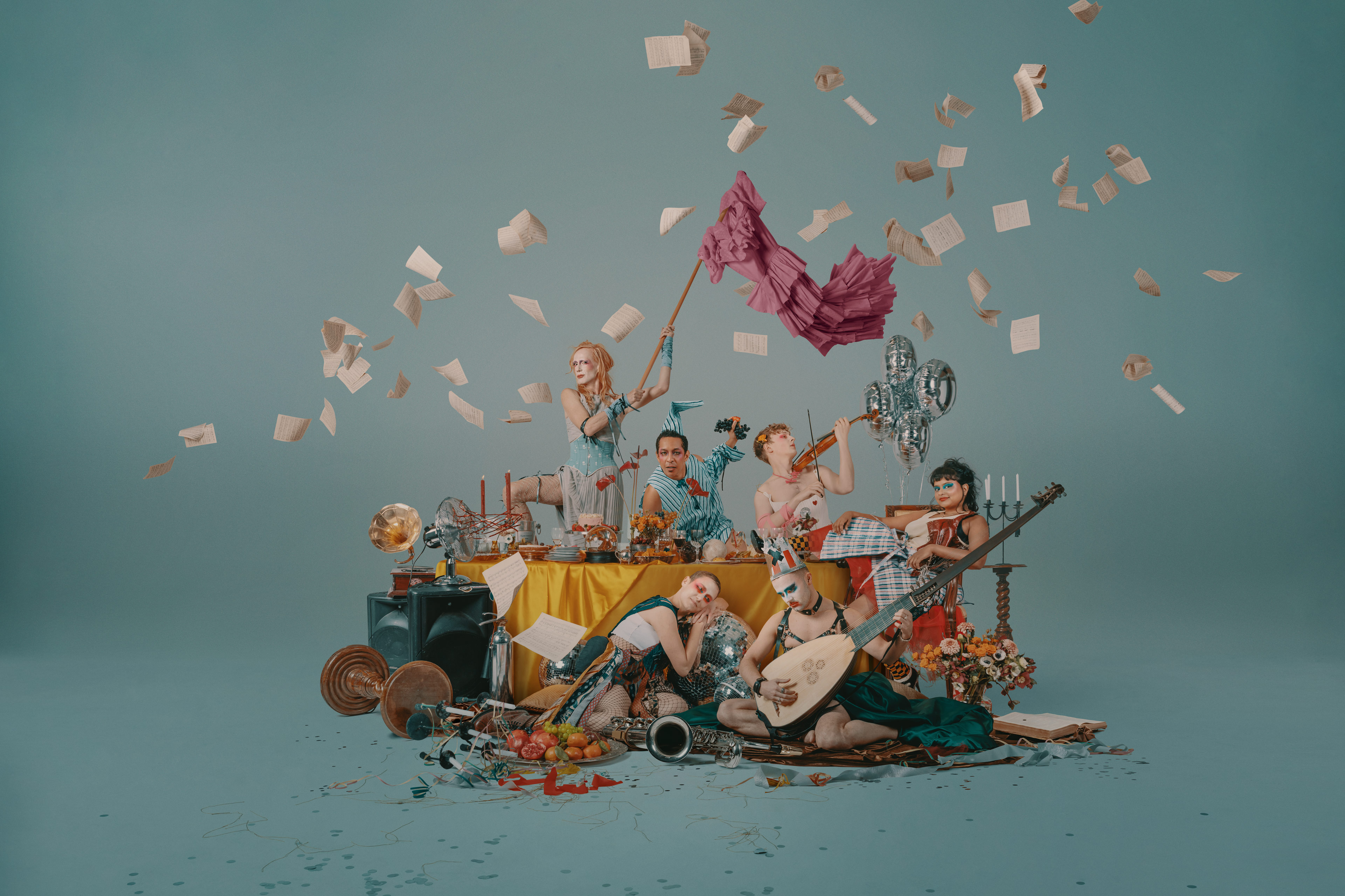 A group of colorfully-costumed characters playing musical instruments, surrounded by an assortment of props.