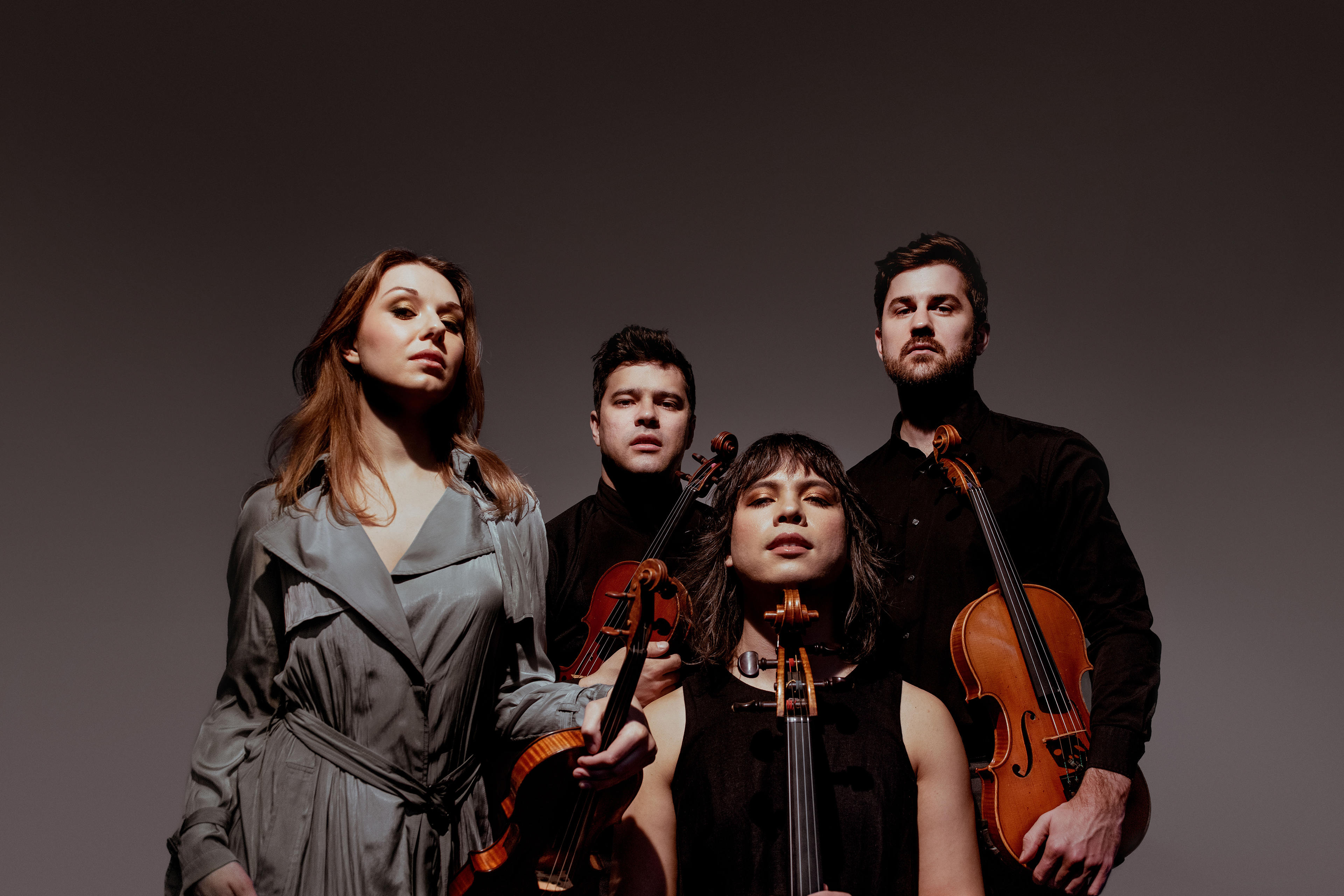 Group headshot of Attacca Quartet musicians wearing dark clothing, their stringed instruments in hand.